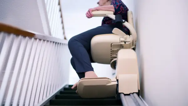 stair-lift-use-residential-home-safe-mobility Person using a stair lift in a residential home to safely travel up a staircase
